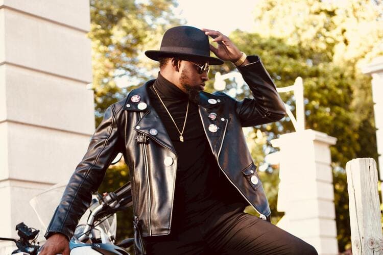 Confident young African American guy leaning on motorbike on street