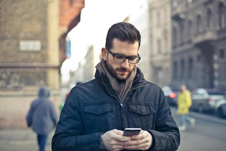 Man Wearing Black Zip Jacket Holding Smartphone Surrounded by Grey Concrete