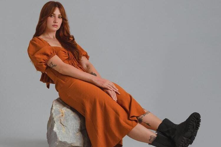 Model in an Orange Midi Dress and Boots Sitting on a Rock