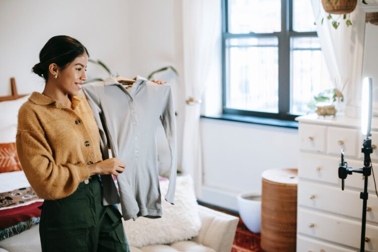 Positive girl posing with her clothes in front of her phone and she records a video.