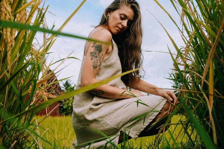 Woman in Loose Fitting Linen Dress Kneeling Among Grass